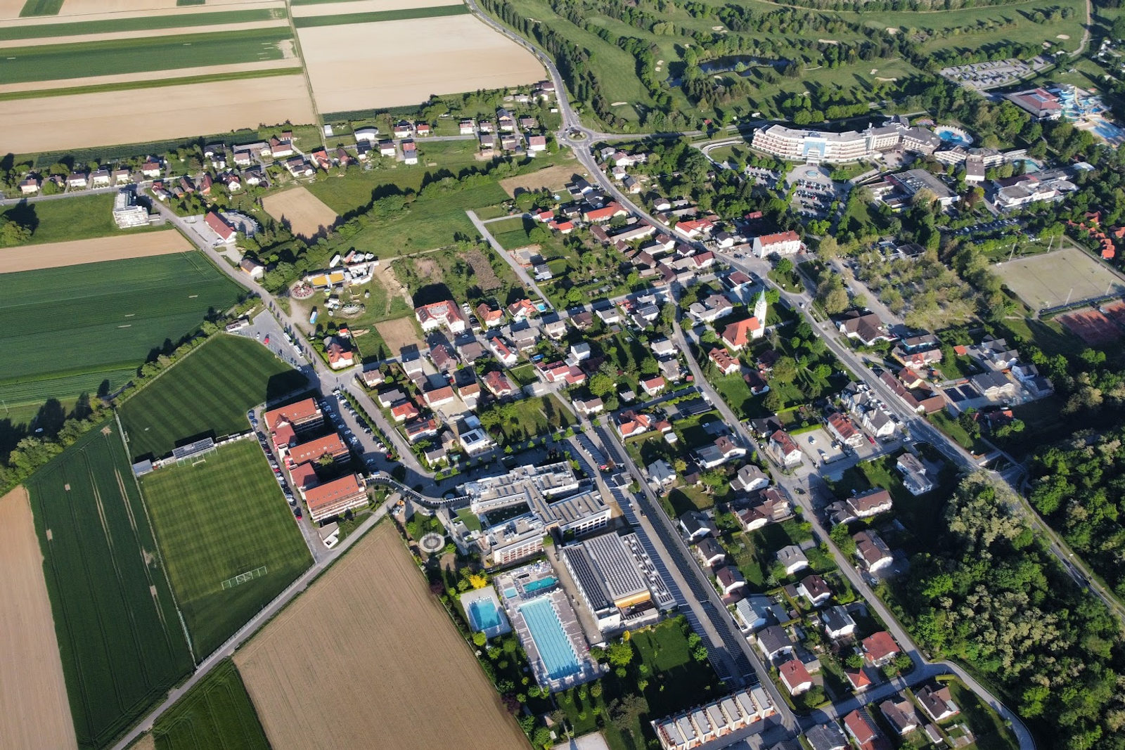 Luftaufnahme des Ortes Moravske Toplice mit Häusern, einer Kirche, Sportplätzen, Freibädern und einem Thermenresort zwischen Bäumen